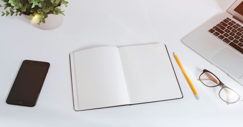 A minimalist workstation with a laptop, open notebook, pencil, and smartphone, set up for outsource content creation.