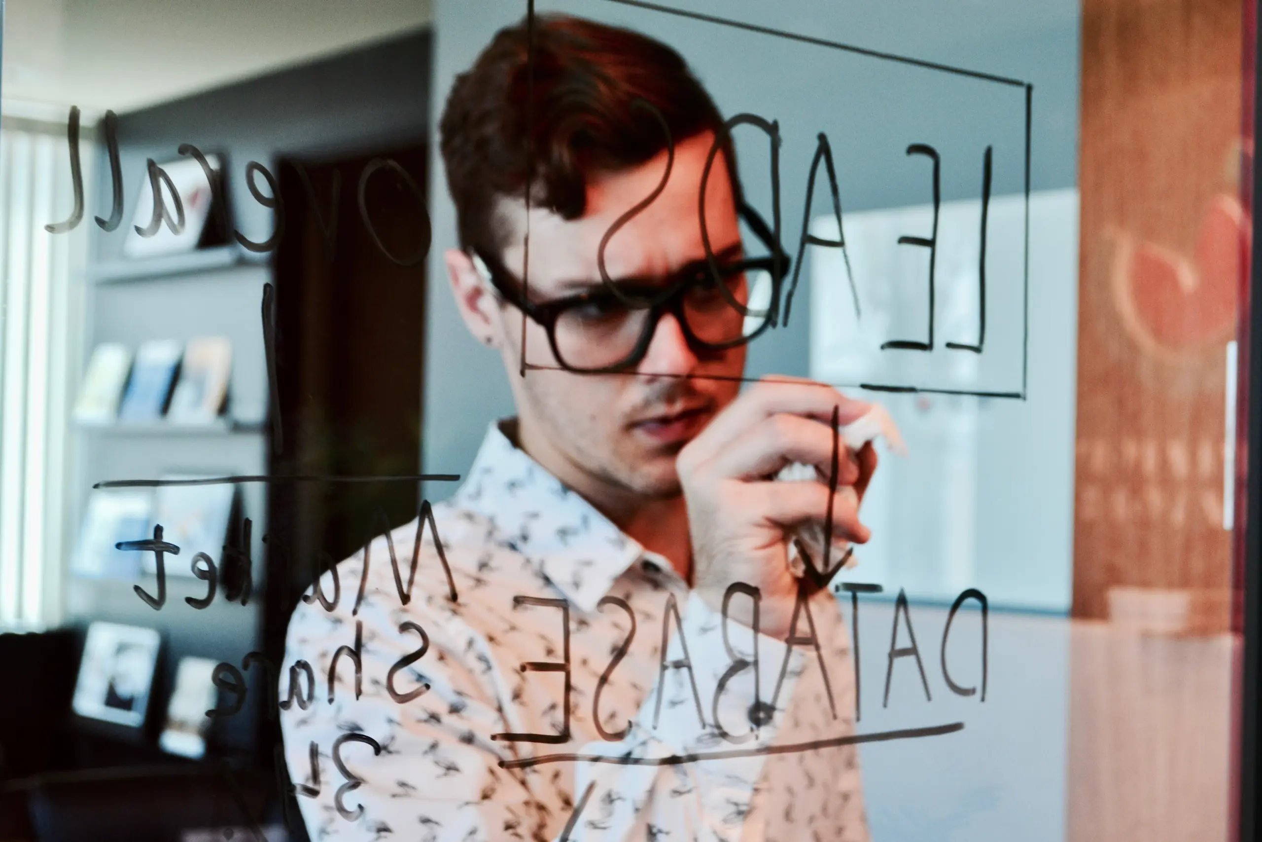 A young marketer writing word Leads on a glass at an office