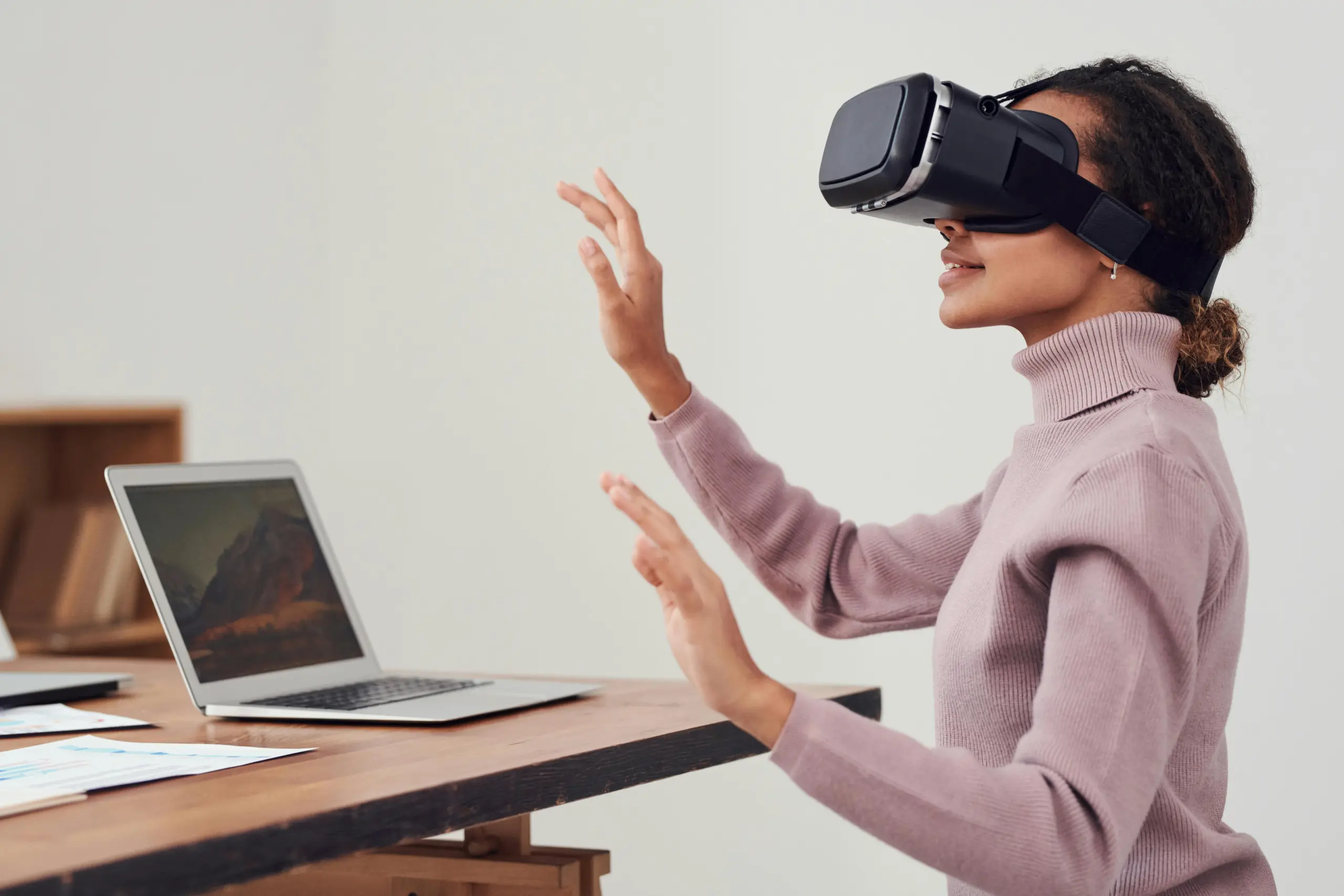 A woman wearing an AR / VR headset with her hands raised at her office desk 