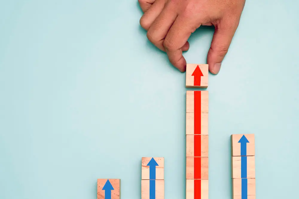 A hand placing a block with an upward arrow on top of a bar graph made of wooden blocks, representing growth in credit union advertising.