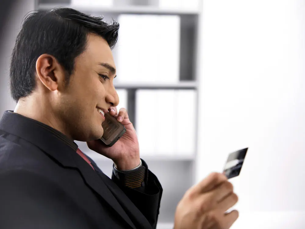 A man on the phone holding a credit card, which could represent a credit union member services representative assisting with a transaction.
