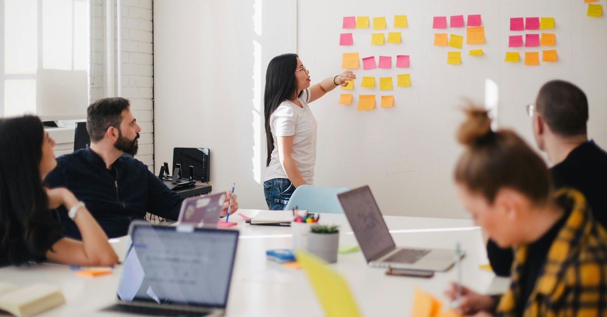 A team collaborates on outsourcing content creation, with a woman pointing at a wall filled with colorful sticky notes.