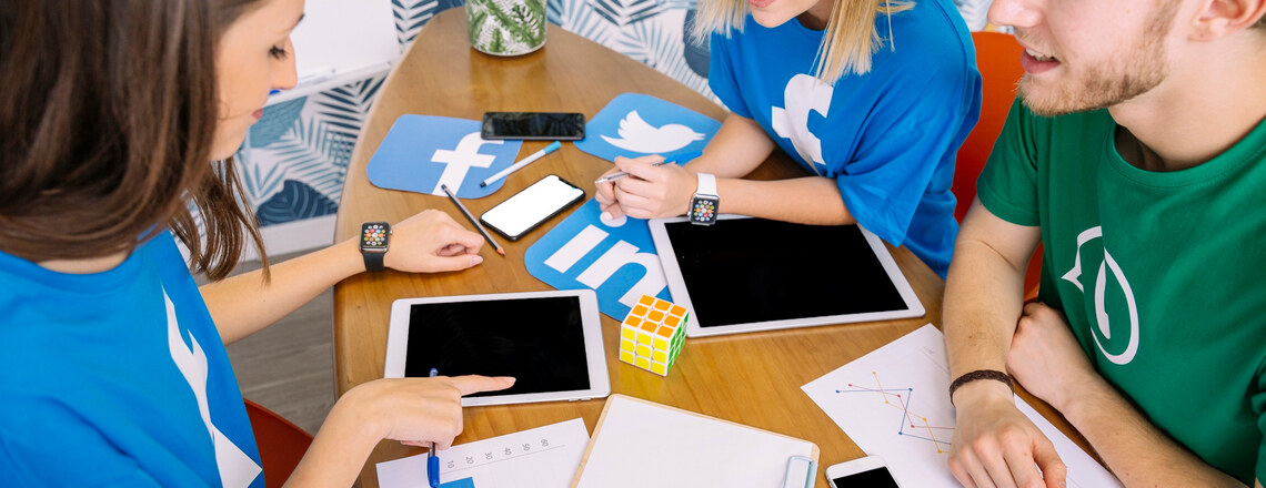 A group of people collaborating at a table with tablets, smartphones, and social media icons, discussing content marketing success metrics.