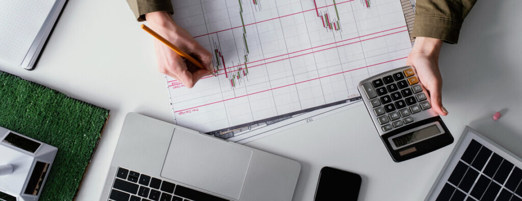 Person analyzing a graph with a calculator and laptop, illustrating the financial impact of stagflation on business profits.