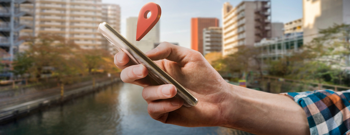 Person using a smartphone with a location pin hovering above it, emphasizing the importance of local SEO for mobile searches.