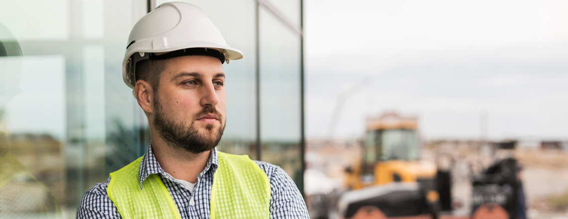 A thoughtful contractor in a safety vest and helmet standing at a construction site, highlighting the challenges of lead generation for contractors.