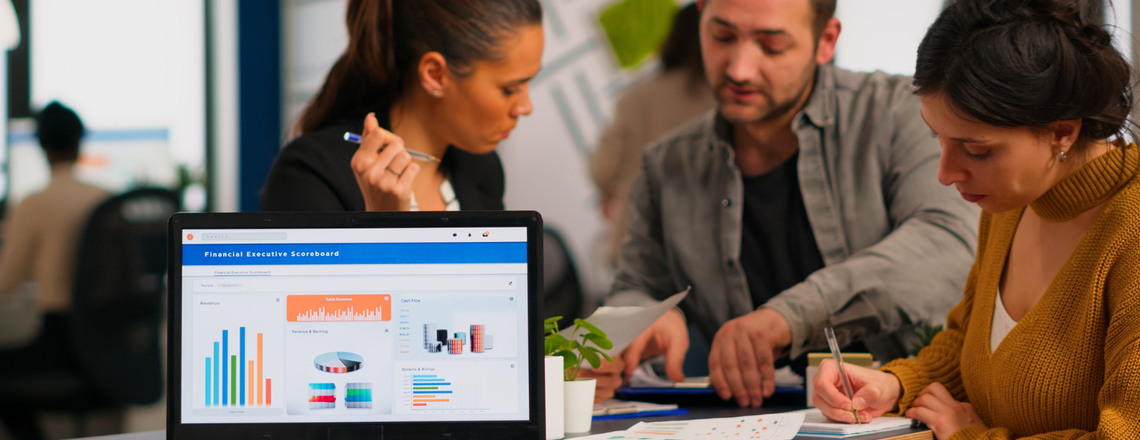 Three colleagues analyze a laptop’s marketing dashboard while discussing lead scoring strategies.